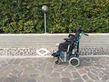 Empty wheelchair on footpath by plants
