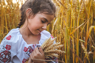 Cute girl holding wheat crops standing on field