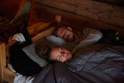 High angle view of couple with blanket sleeping on bed in cottage