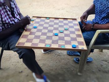 Men playing wooden chess on a bench.