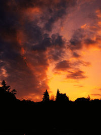 Silhouette trees against dramatic sky during sunset