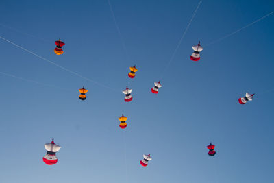 Low angle view of kites flying against clear blue sky