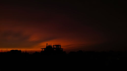 Silhouette built structure against dramatic sky during sunset