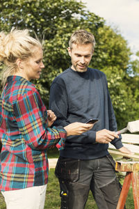 Woman showing phone to male worker while working at farm