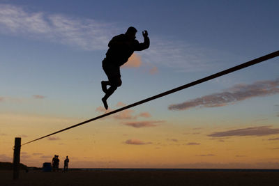 Silhouette man jumping in sea against sky during sunset