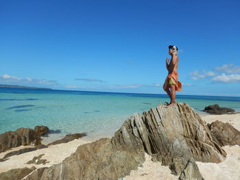 Woman standing on rock at beach against clear blue sky