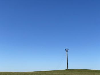 Electricity pylon on field against clear blue sky