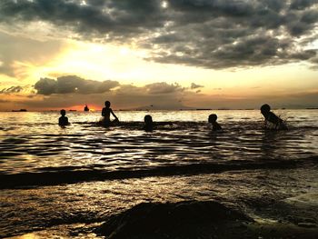 Silhouette people on beach against sky during sunset