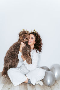 Portrait of young woman sitting with dog and balloons on floor at home