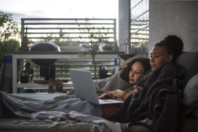 Mother and daughter watching laptop while relaxing on sofa at home