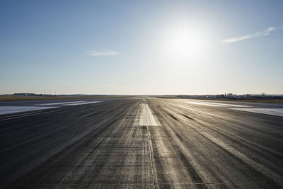 Surface level of long airport runway with directional marking against clear sky.