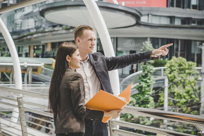 Colleagues discussing file while standing on footbridge