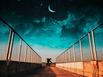 Man jumping on bridge against sky