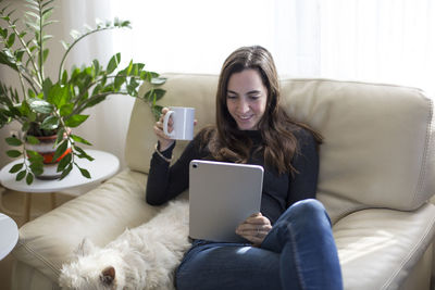 Young woman using phone while sitting on sofa