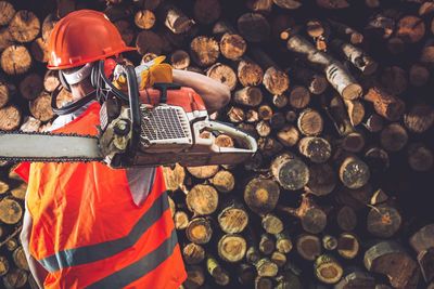 Rear view of manual worker holding power tool while standing in lumber industry