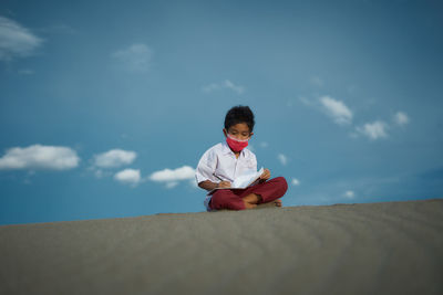 Portrait of boy sitting against sky