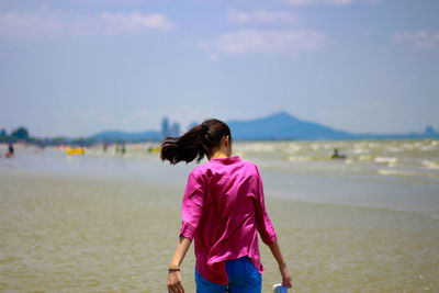 Rear view of woman standing on beach against sky