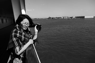 Man photographing with arms raised standing at sea shore against clear sky