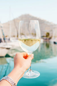 Woman hand with white wine, champagne glass on yachts, sailing boats background. nice, france.