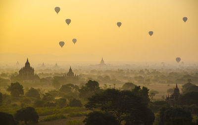 Hot air balloons flying over city against clear sky during sunrise