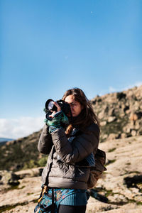 Young woman photographing against blue sky