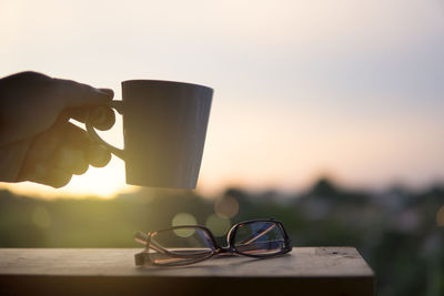 Close-up of hand holding drink against sky during sunset