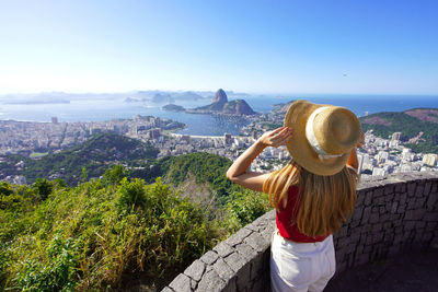 Stylish girl holding hat on rio de janeiro viewpoint with guanabara bay, rio de janeiro, brazil