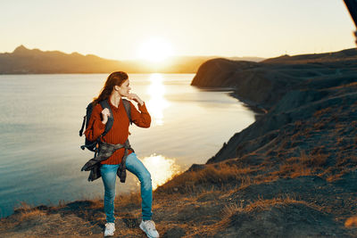 Man standing on rock by sea against sky during sunset