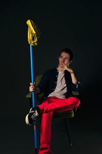 Thoughtful fashion model sitting with mop on chair against gray background