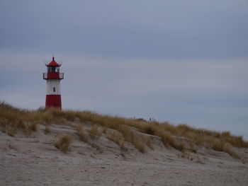 Lighthouse on beach by sea against sky