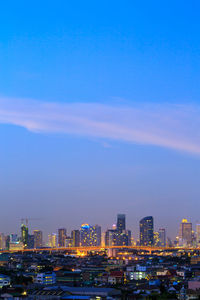 Illuminated buildings in city against blue sky