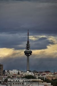 Communications tower in city against sky during sunset
