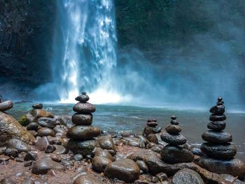 Stones stacked by river against waterfall