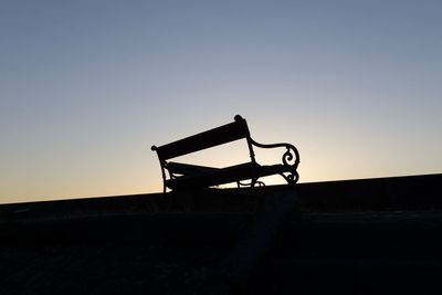 Silhouette bench against clear sky during sunset