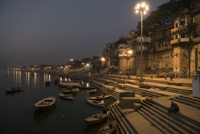 Boats moored on illuminated city by sea against sky at night