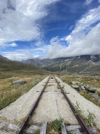 Railroad track leading towards mountains against sky