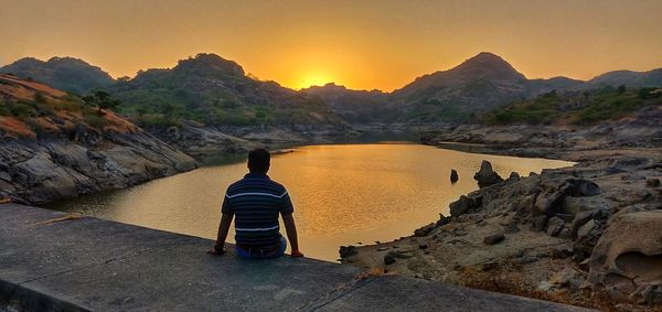 Rear view of man looking at view of mountain during sunset