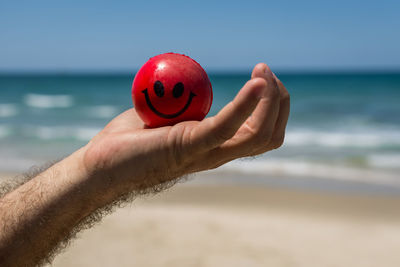 Close-up of hand holding red ball against beach