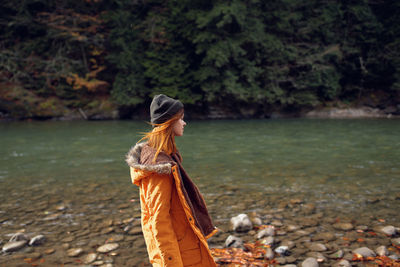 Rear view of woman standing on rock by lake