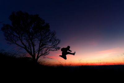 Silhouette man jumping on field against sky at sunset