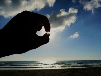 Close-up of hand against sea at sunset