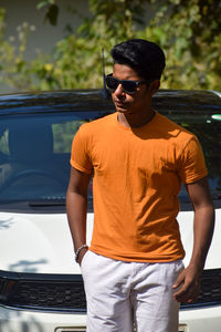 Portrait of young man standing against car