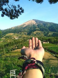 Midsection of person hand on mountain against sky