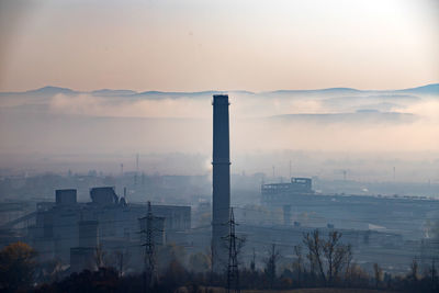 Smoke emitting from factory against sky during sunset