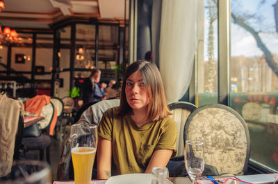 A young black-haired girl sits in a cafe and there is a glass of beer in front of her