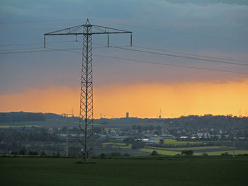 Electricity pylons on field at sunset