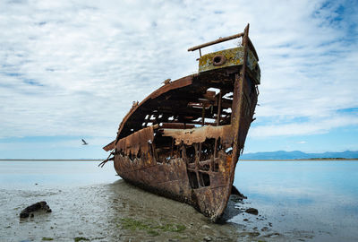 Abandoned boat at beach against sky