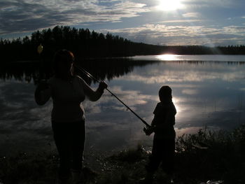 Rear view of silhouette man and woman fishing at lake