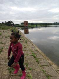 Girl standing on lake shore against sky