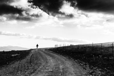 Man standing on road amidst agricultural field against sky